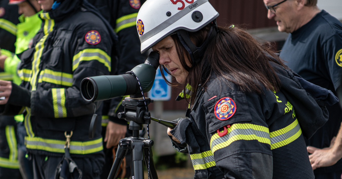 En grupp brandmän som står bredvid varandra. En tittar i en kikare.