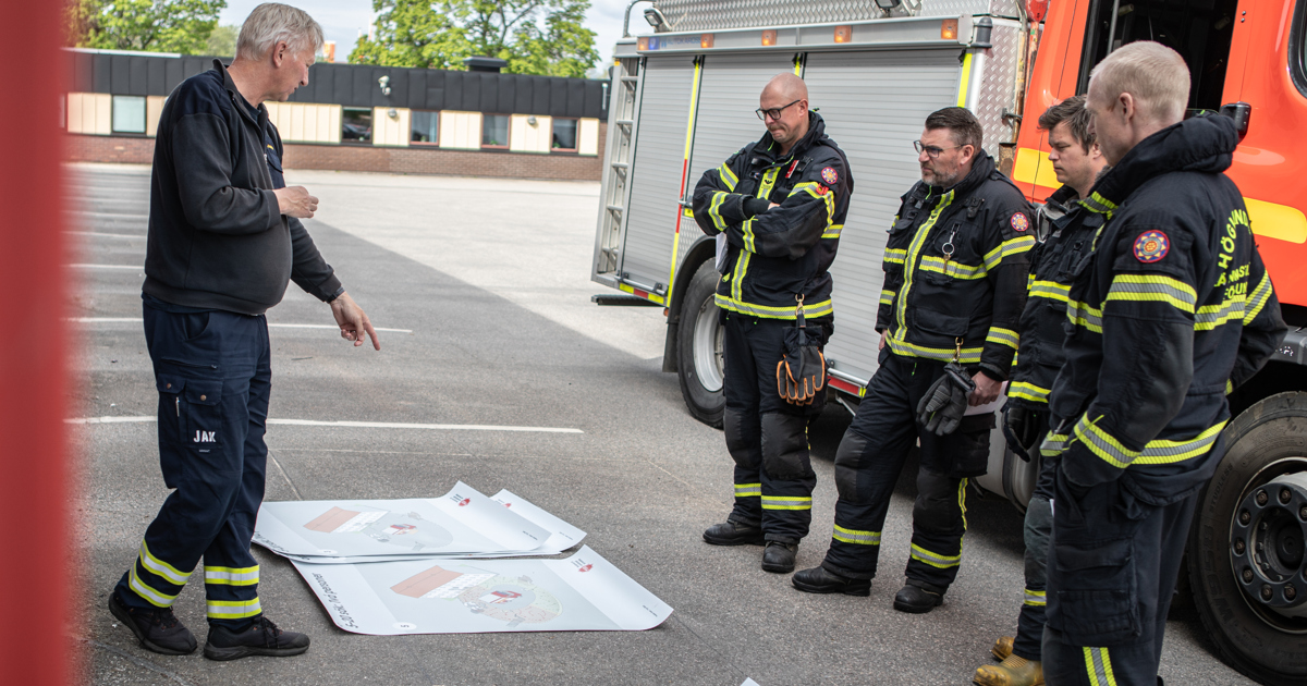 En grupp brandmän står bredvid varandra nära en brandbil.